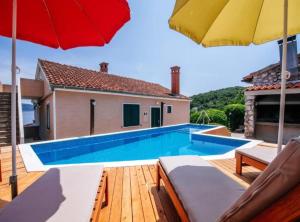 a swimming pool with a red and yellow umbrella at Holiday Home Villa Rokov in Mali Iž