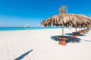 een rij banken op een strand met een rieten parasol bij La Casa sulla Spiaggia Torre San Giovanni in Torre San Giovanni Ugento