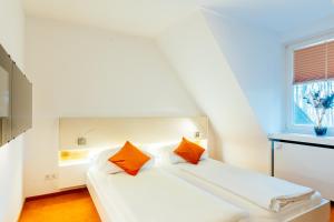 ein weißes Bett mit orangefarbenen Kissen in einem Zimmer in der Unterkunft Heideblick - Tagungs- und Freizeithotel an der Lüneburger Heide in Jesteburg