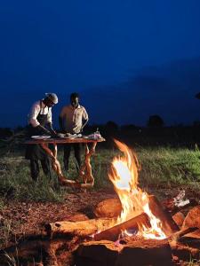 Twee mannen zitten aan een picknicktafel naast een vuur. bij Veilscape Mara Camp in Masai Mara