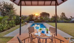 a patio with a table and chairs next to a pool at SaffronStays Green Lawns in Pāli