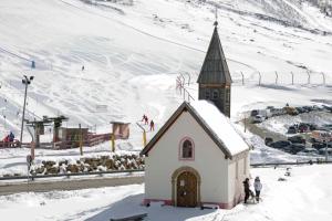 a small church in the snow next to a mountain at Sporthotel Kurzras in Maso Corto +1 photo