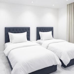 2 bedden met witte lakens en kussens in een kamer bij Najd Cozy Apartment in Dammam
