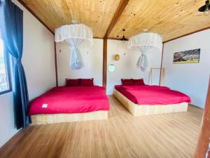 two beds in a room with red sheets and wood floors at Nhà Dâu Homestay in Muong Cha