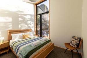 een slaapkamer met een bed, een raam en een stoel bij Trails End - Architectually designed retreat in Punakaiki