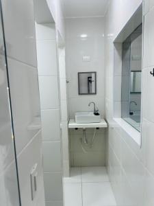 een witte badkamer met een wastafel en een spiegel bij Pousada Montblanc suíte 4 in Guarujá