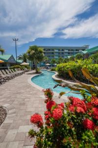a resort swimming pool with red flowers in front of a building at Beachside Hotel & Suites Cocoa Beach - Port Canaveral in Cocoa Beach