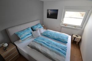 een wit bed met blauwe kussens en een raam bij Wohnen bei Gerlis - DZ 106 in Burbach