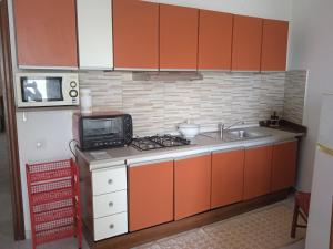een keuken met oranje kasten, een wastafel en een magnetron bij appartamento Gabry in Dolianova