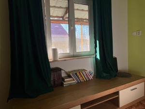 een raam met groene gordijnen en boeken op een houten tafel bij Popasul din Valea Mare in Caransebeş