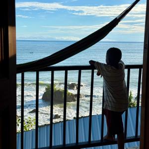 un ragazzino in piedi su un balcone che guarda l'oceano di Altos de la Playa a Bahía Solano