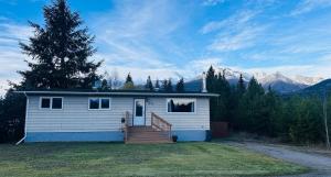 a small white house with a staircase in a yard at Mountain Joy Getaway in Valemount