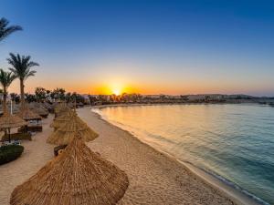 ein Strand mit Strohschirmen und das Meer bei Sonnenuntergang in der Unterkunft Movenpick Resort El Quseir in Al-Qusair