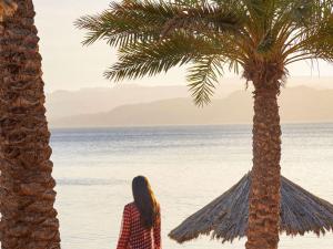 a woman standing next to a palm tree on the beach at Mövenpick Resort & Residences Aqaba in Aqaba