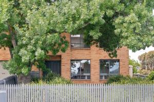 a brick house behind a white fence with a tree at Spacious beachside family home in Rosebud