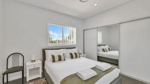 een witte slaapkamer met twee bedden en een raam bij Bella Callala in Callala Beach