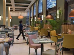 a person walking through a restaurant with tables and chairs at Pullman Nairobi Upper Hill in Nairobi