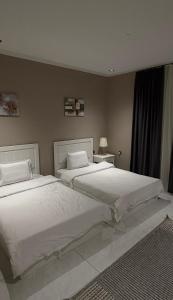 twee witte bedden in een slaapkamer met twee tafels bij شاليهات لورين الفندقية in Taif
