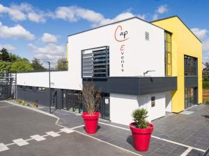 ein Gebäude mit zwei Topfpflanzen auf einem Parkplatz in der Unterkunft ibis Rennes Beaulieu in Cesson-Sévigné