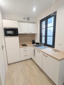 een keuken met witte kasten en een groot raam bij Studio cosy et équipé proche Paris in Saint-Leu-la-Forêt