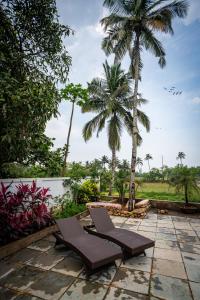 a patio with two lounge chairs and palm trees at Mistral by the sea in Benaulim