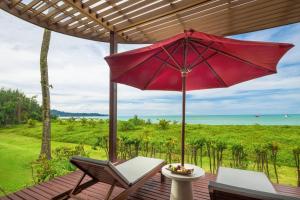 a red umbrella on a deck with chairs and a table at Ramada Resort by Wyndham Khao Lak in Khao Lak