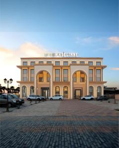 ein großes Gebäude mit auf einem Parkplatz abgestellten Autos in der Unterkunft The Madelinne Hotel in Muzaffarnagar