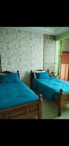 two beds with blue sheets in a bedroom at บ้านพักสายรุ้ง เพรชรบุรี in Tha Chang