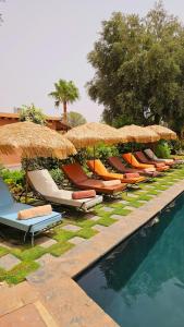 een rij ligstoelen en parasols naast een zwembad bij L'oasis de paix in Aït Amara