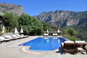 une piscine avec des chaises longues et une montagne dans l'établissement Kabak Avalon Bungalows, à Faralya