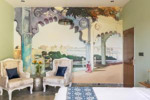 a bedroom with two chairs and a mural at SaffronStays Grand Pavilion in Udaipur