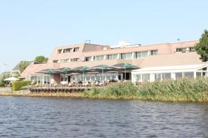 ein Restaurant mit Tischen und Sonnenschirmen neben dem Wasser in der Unterkunft Hotel Zwartewater in Zwartsluis
