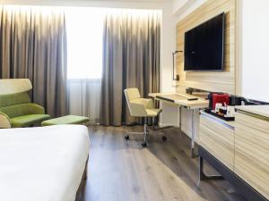 een hotelkamer met een bureau en een tv bij Novotel Sevilla in Sevilla
