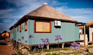 une petite maison avec un toit de chaume et des fleurs violettes dans l'établissement Cabañas Las Achiras, à Punta del Diablo