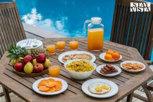 - une table en bois avec des aliments pour le petit-déjeuner et du jus d'orange dans l'établissement StayVista at Thalassa Near The Beach, à Alibaug