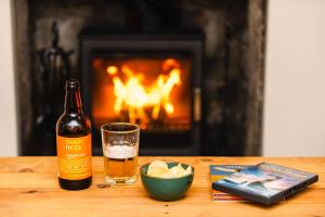 a bottle of beer and a glass on a table with a fireplace at Crossroads Cottage in Drumnadrochit