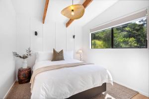 a white bedroom with a bed and a window at Tui & Nikau Cabins in Mangawhai