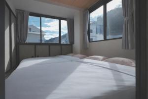 een slaapkamer met 2 witte bedden en 2 ramen bij AURA YUZAWA Apartment Hotel - 1Bedroom Apartment with Living Dining Kitchen Sleeps 2 to 4, Bedroom with 2-Double Bed, Living Room with 1-Sofa Bed in Yuzawa