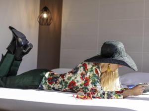 une femme portant un chapeau allongée dans une baignoire avec un téléphone portable dans l'établissement ibis styles Trani, à Trani