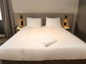 een groot wit bed met een witte handdoek erop bij Blooma Hotel Liege Centre - Handwritten Collection in Luik