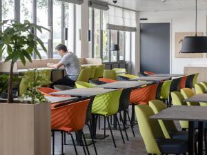 een man zit aan een tafel in een cafetaria met kleurrijke stoelen bij ibis Styles Almere in Almere