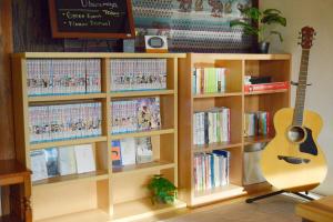een boekenplank gevuld met boeken en een gitaar bij 宇都宮ゲストハウス花ニ嵐 in Utsunomiya