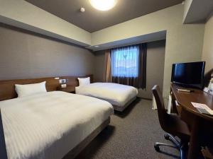 ein Hotelzimmer mit zwei Betten und einem Schreibtisch und einem Fernseher in der Unterkunft Hotel Route-Inn Shiojiri in Shiojiri + 29 Fotos