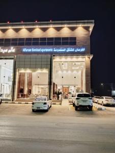 two cars parked in front of a store at night at الفرسان للشقق المخدومه in Al Kharj