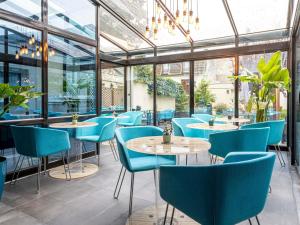 un restaurant avec des chaises, des tables et des fenêtres bleues dans l'établissement Mercure Paris Malakoff Parc des Expositions, à Malakoff