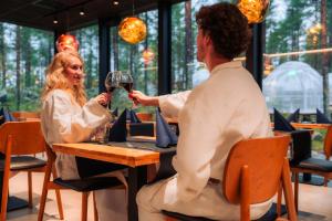 een man en vrouw die aan een tafel wijn drinken bij Aurora Igloo, Sauna Spa & Dinner by Invisible Forest Lodge Adults Only in Rovaniemi