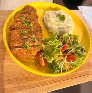 a yellow plate of food with meat and salad on a table at Pupa Women Hostel in Patong Beach