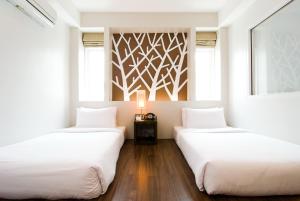 two beds in a room with white walls and wood floors at The Album Hotel in Patong Beach