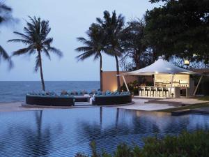a swimming pool with a tent and palm trees and the ocean at Mövenpick Asara Resort & Spa Hua Hin in Hua Hin