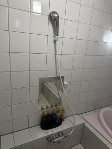 een douche in een badkamer met witte tegels en flessen bij ホテルemoemo in Fuchu